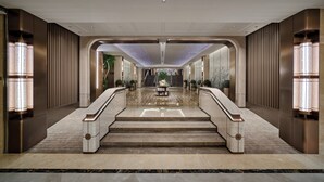 Un lobby de hotel moderno y espacioso con una escalera de mármol que conduce a un ascensor.