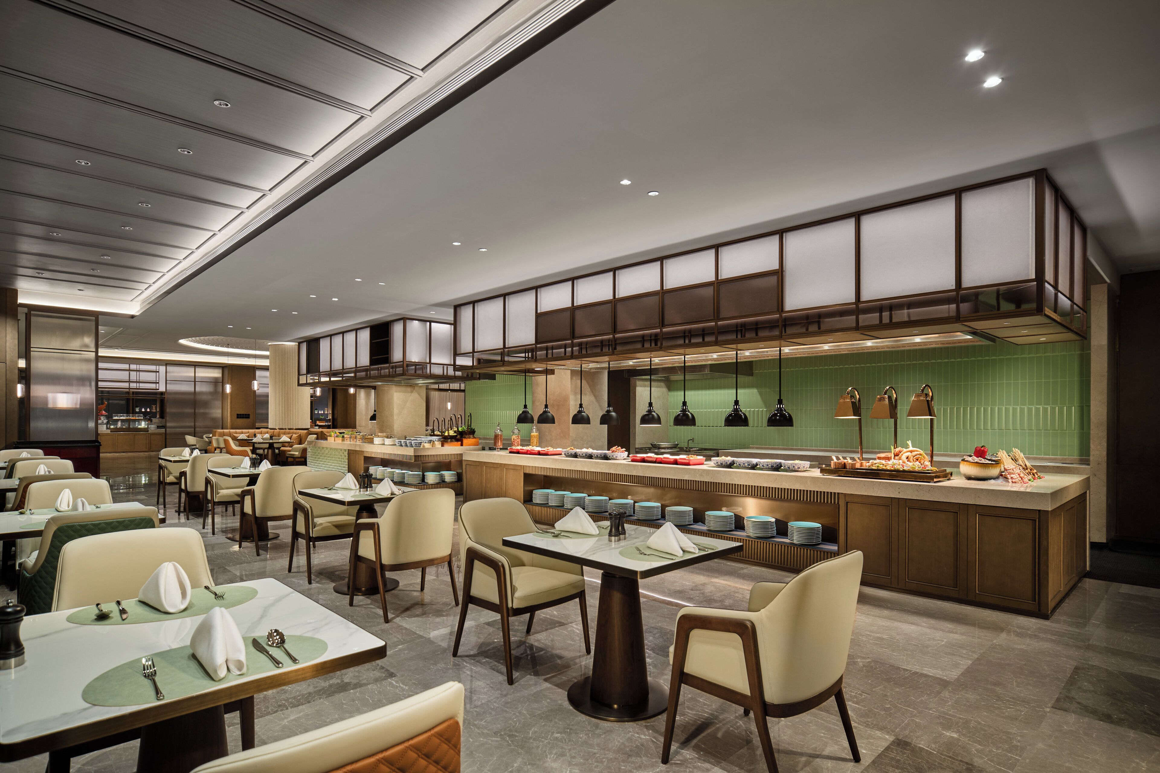 Un restaurant moderne doté d’un îlot central, de plusieurs tables et d’un plafond haut avec des luminaires encastrés.