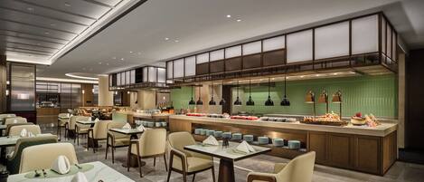 Un restaurant moderne doté d’un îlot central, de plusieurs tables et d’un plafond haut avec des luminaires encastrés.