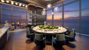 A modern dining area with a round table set for six, surrounded by chairs, with a city view through large windows. - Intercontinental Huzhou Taihu South By Ihg (Huzhou)