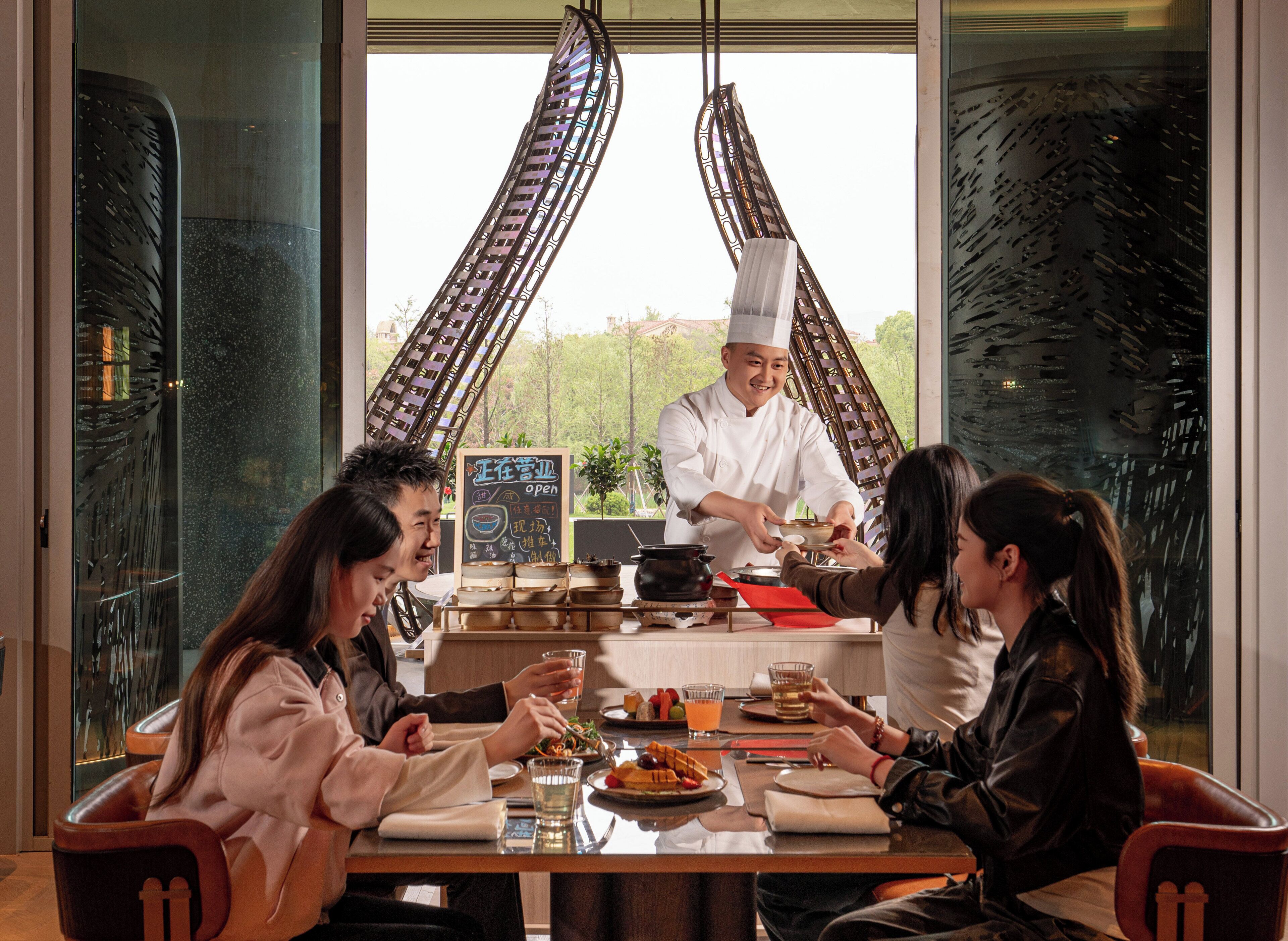 A restaurant with a chef serving food to customers at a table.