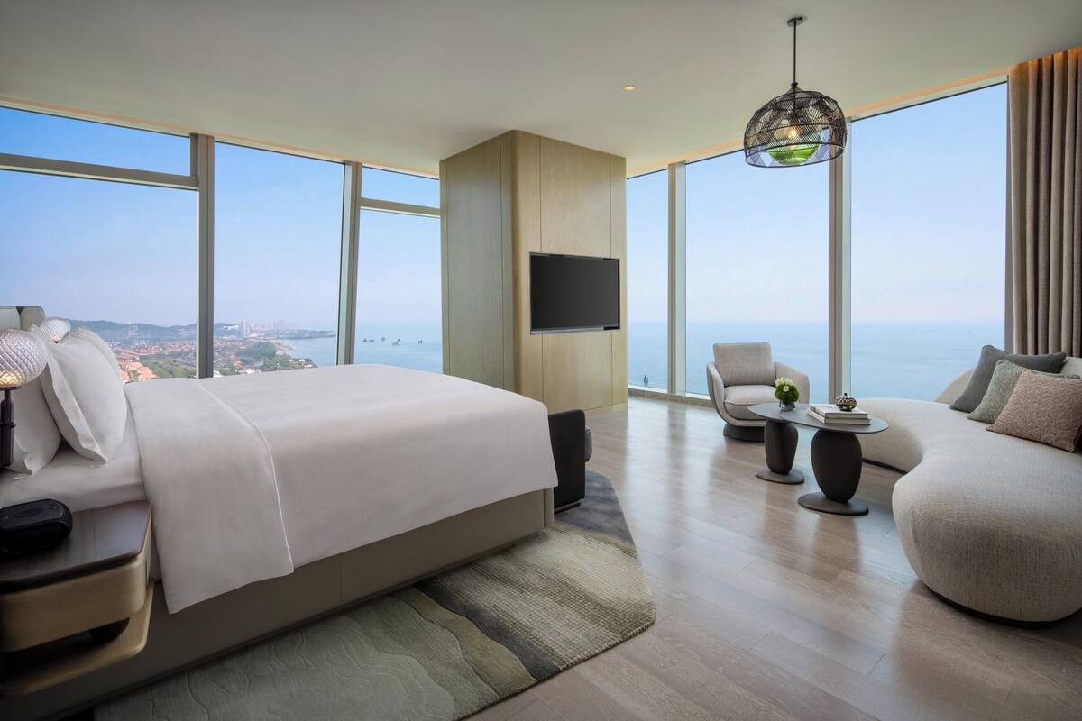 Ein modernes Hotelzimmer mit einem großen Bett, einem Fernseher, einer Couch und Meerblick.