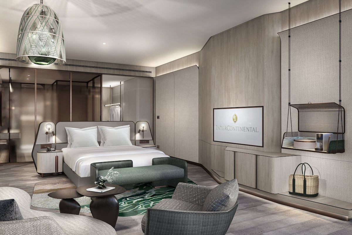 Ein modernes Hotelzimmer mit einem großen Bett, zwei Nachttischen mit Lampen, einer Sitzecke mit einer Couch und Sesseln, einer hängenden Leuchte und einem wandmontierten Fernseher.