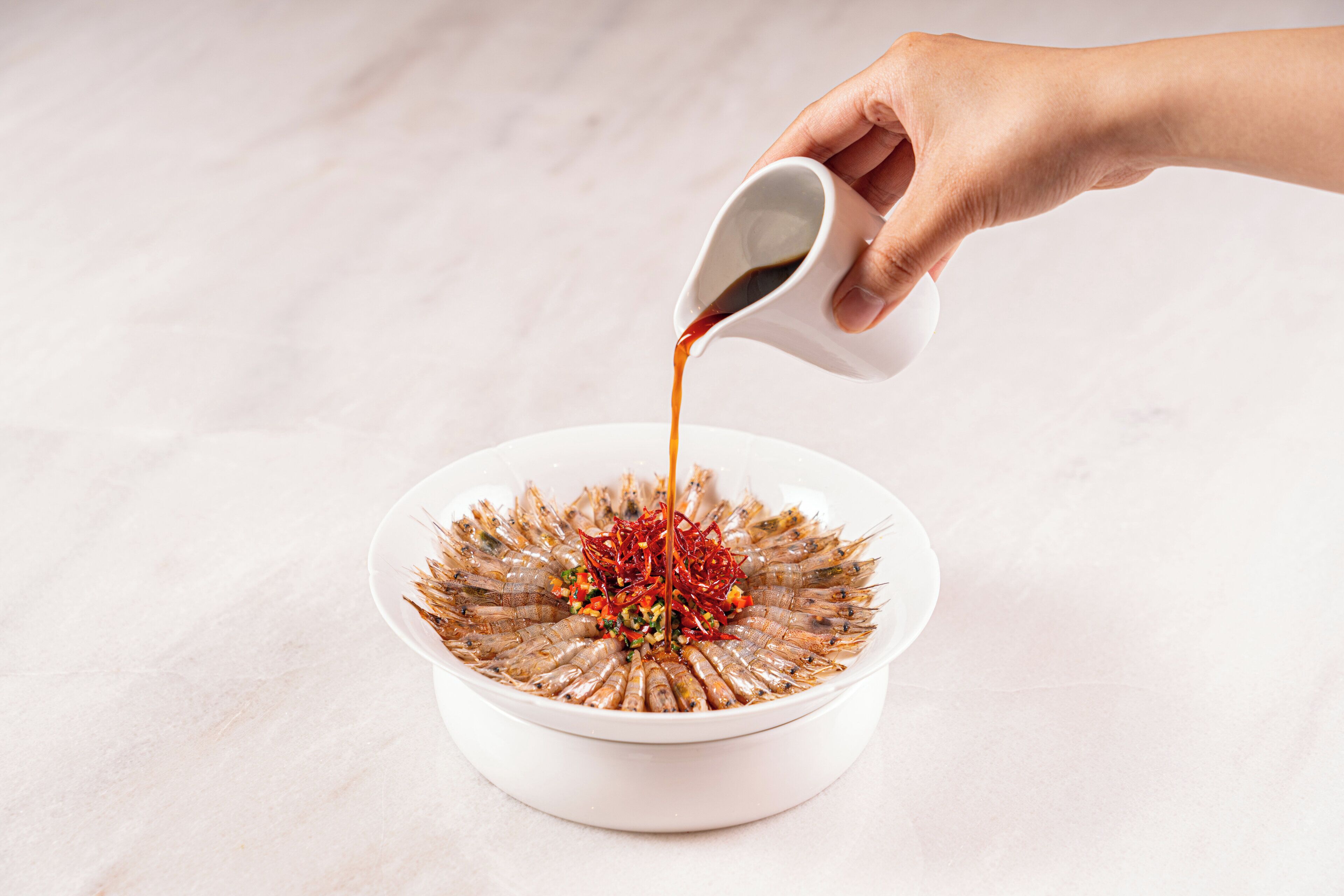 A hand pouring sauce over a dish of food.