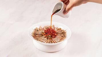 A hand pouring sauce over a dish of food.
