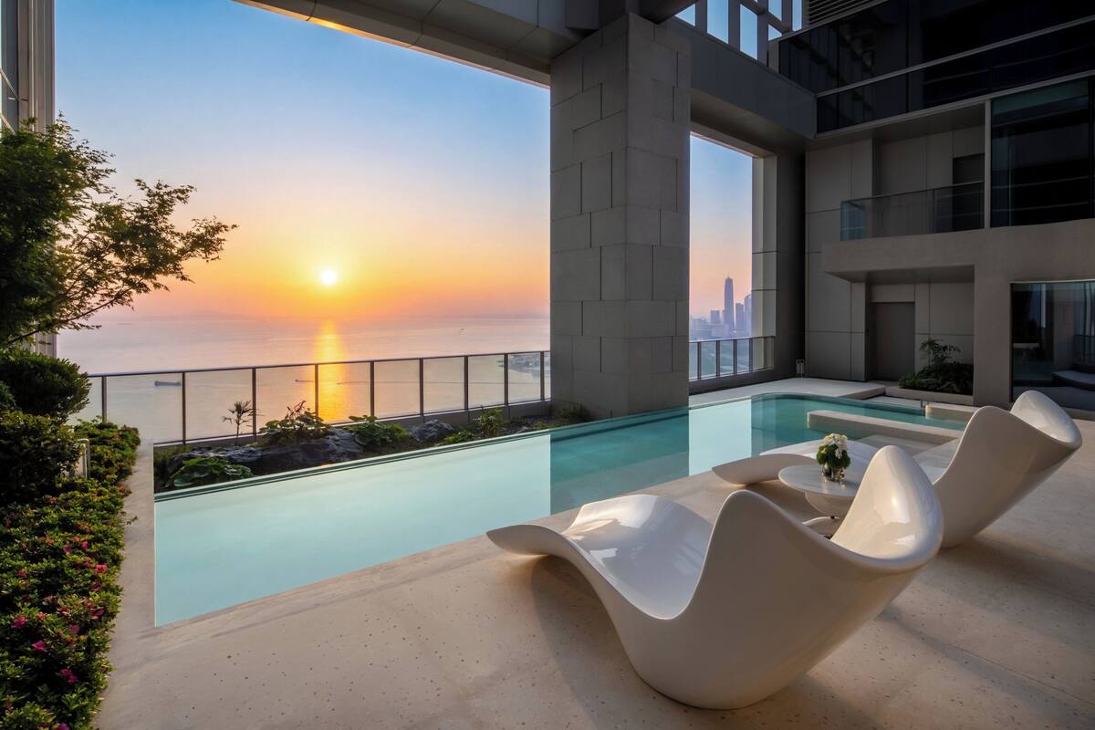 Ein moderner Poolbereich im Innenbereich mit Blick auf einen Sonnenuntergang, zeitgemäße Liegestühle und eine Stadtlandschaft im Hintergrund.