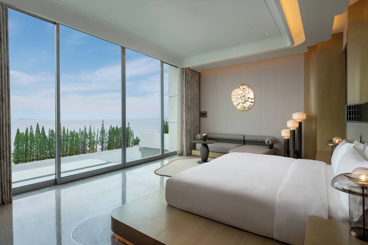 Ein modernes Hotelzimmer mit einem großen Bett, einer Sitzecke und Blick ins Freie.