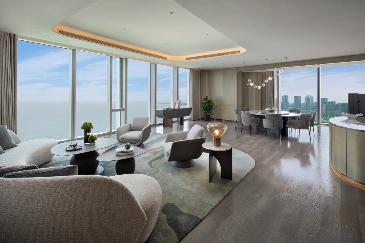 A modern hotel room with a large window, a dining area, and a seating area with a view of the city.