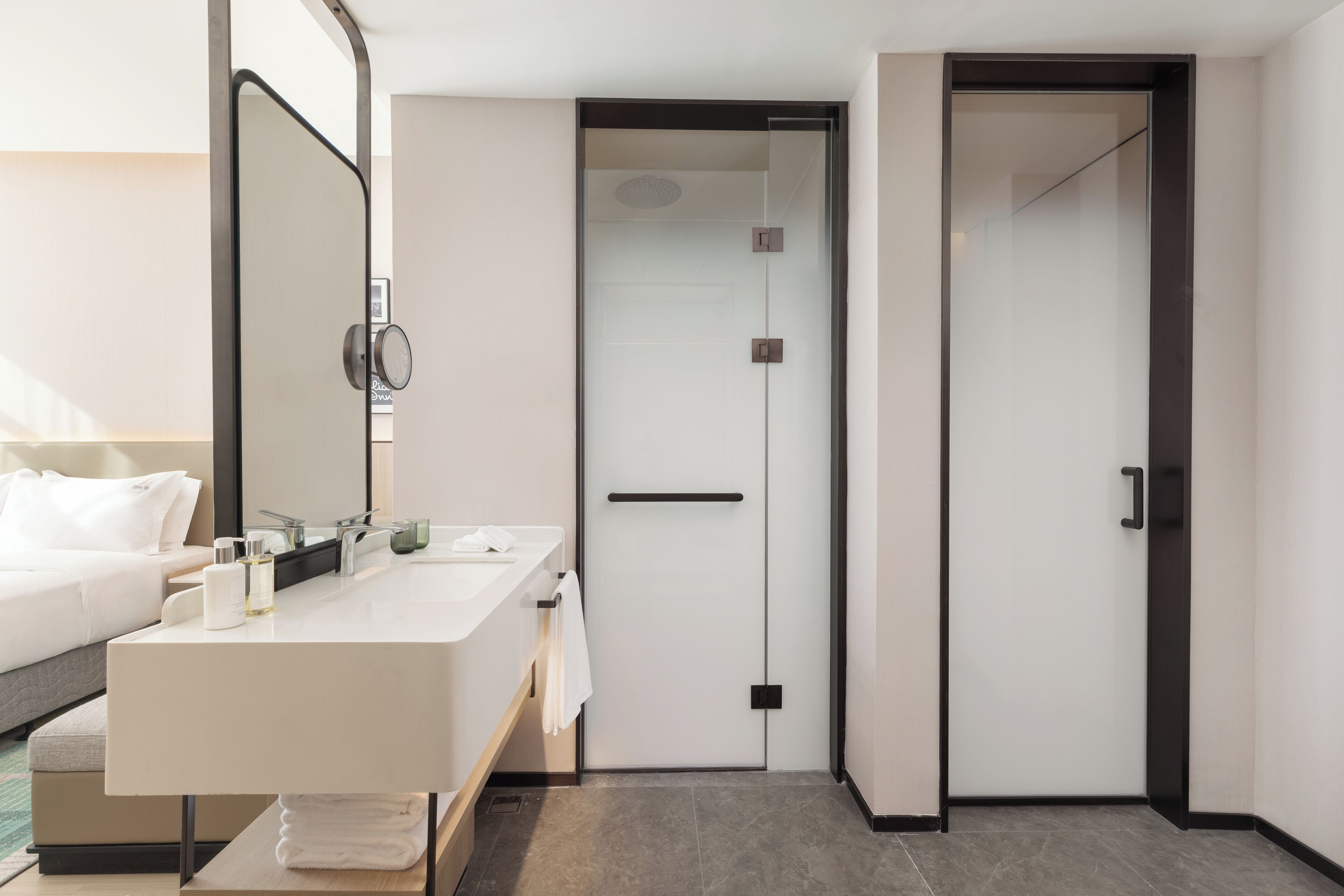 A modern hotel room with a large bed, a double sink, and a separate shower area.
