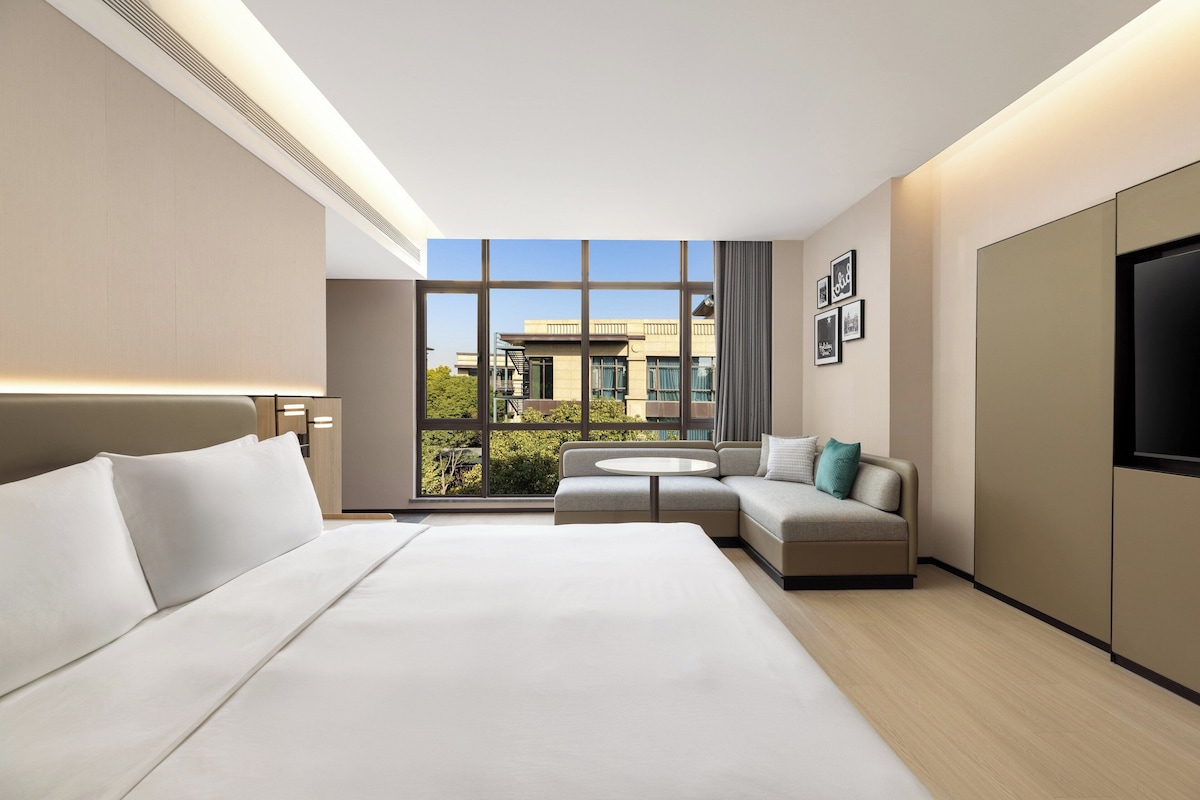 Una habitación de hotel moderna con una cama grande, un sofá, una mesita redonda y un televisor.