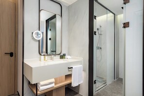 Un baño moderno con un espejo grande, un lavabo blanco y una ducha con mampara de vidrio.