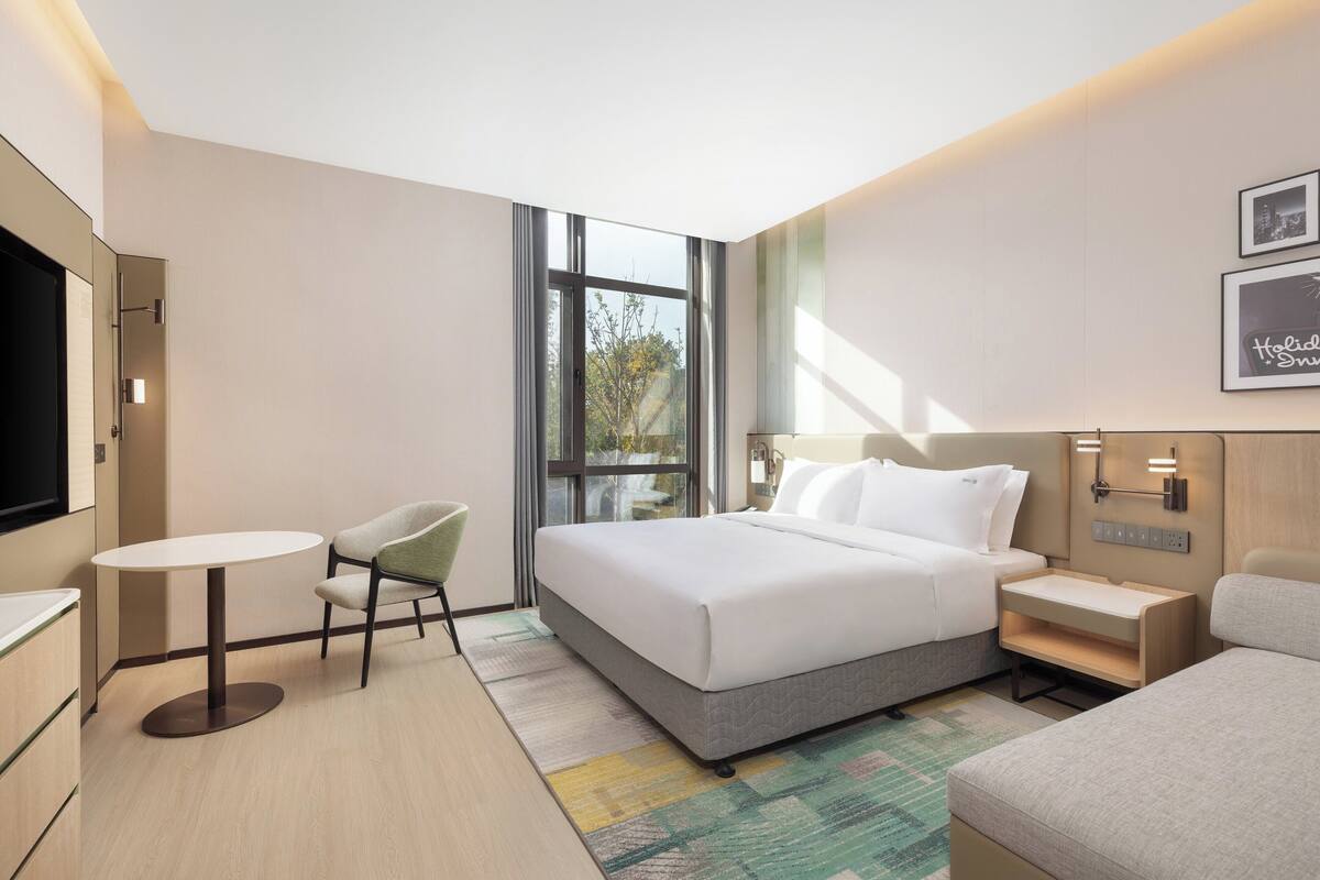 A modern hotel room with a large bed, a small table, a chair, and a TV.