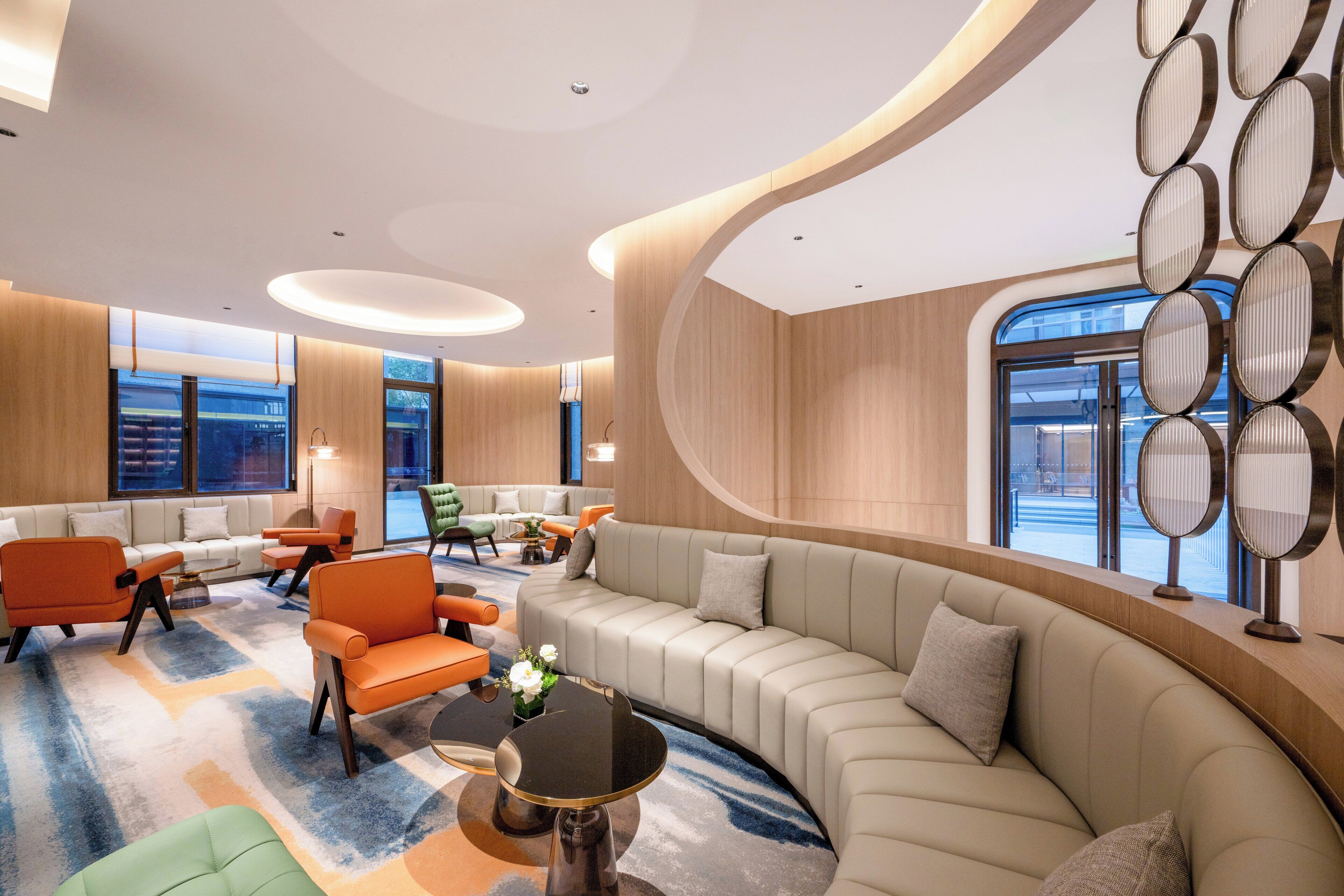 A modern hotel lobby with a curved seating area, large windows, and a decorative wall.