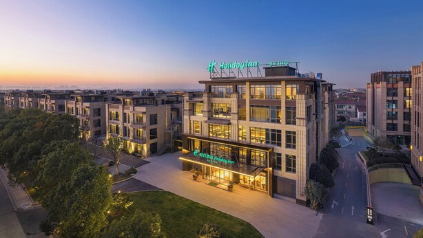 Un moderno hotel Holiday Inn con una terraza en la azotea y una entrada bien iluminada.