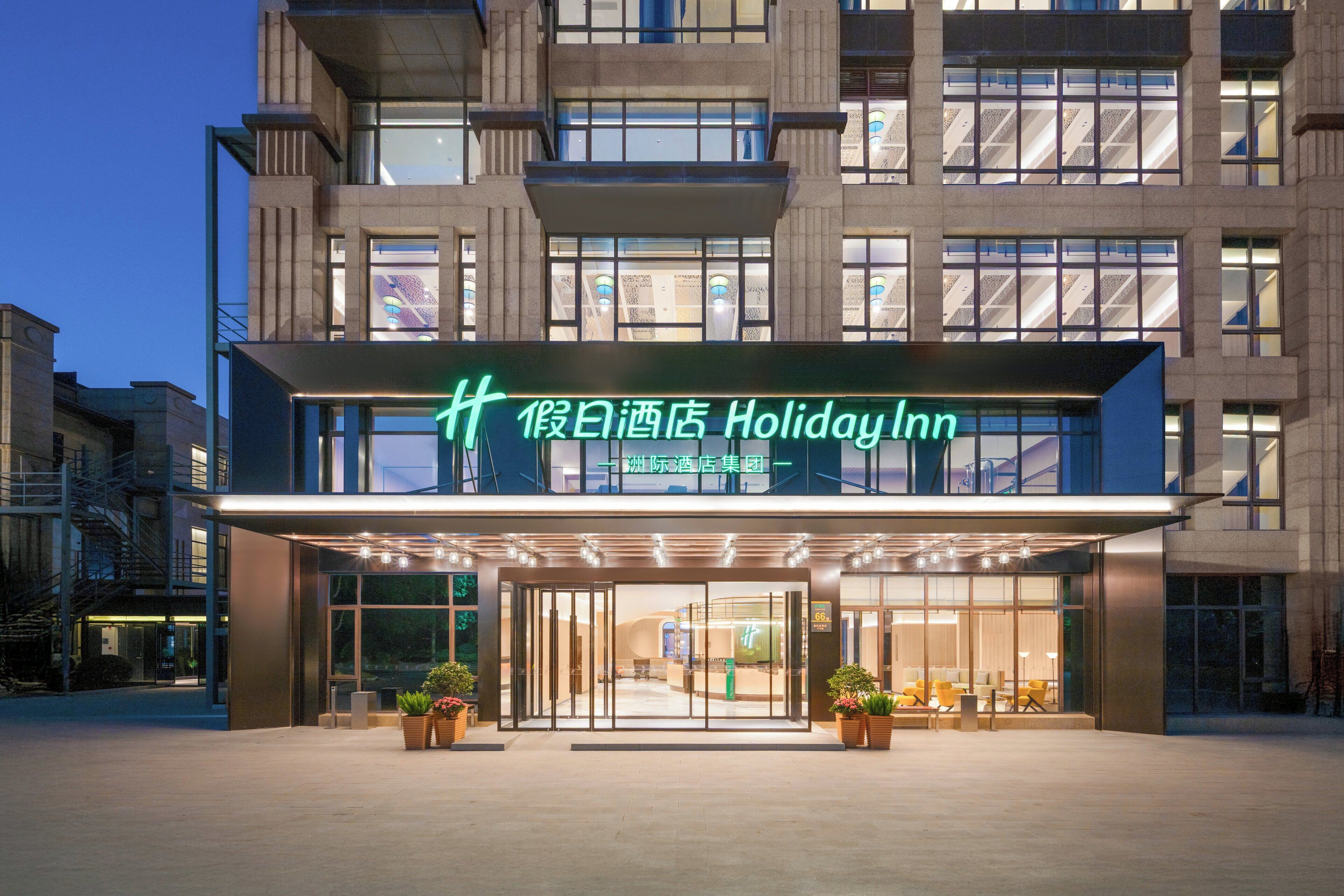 Entrada de un hotel Holiday Inn con fachada moderna, amplios ventanales y una zona de acceso acogedora con asientos.