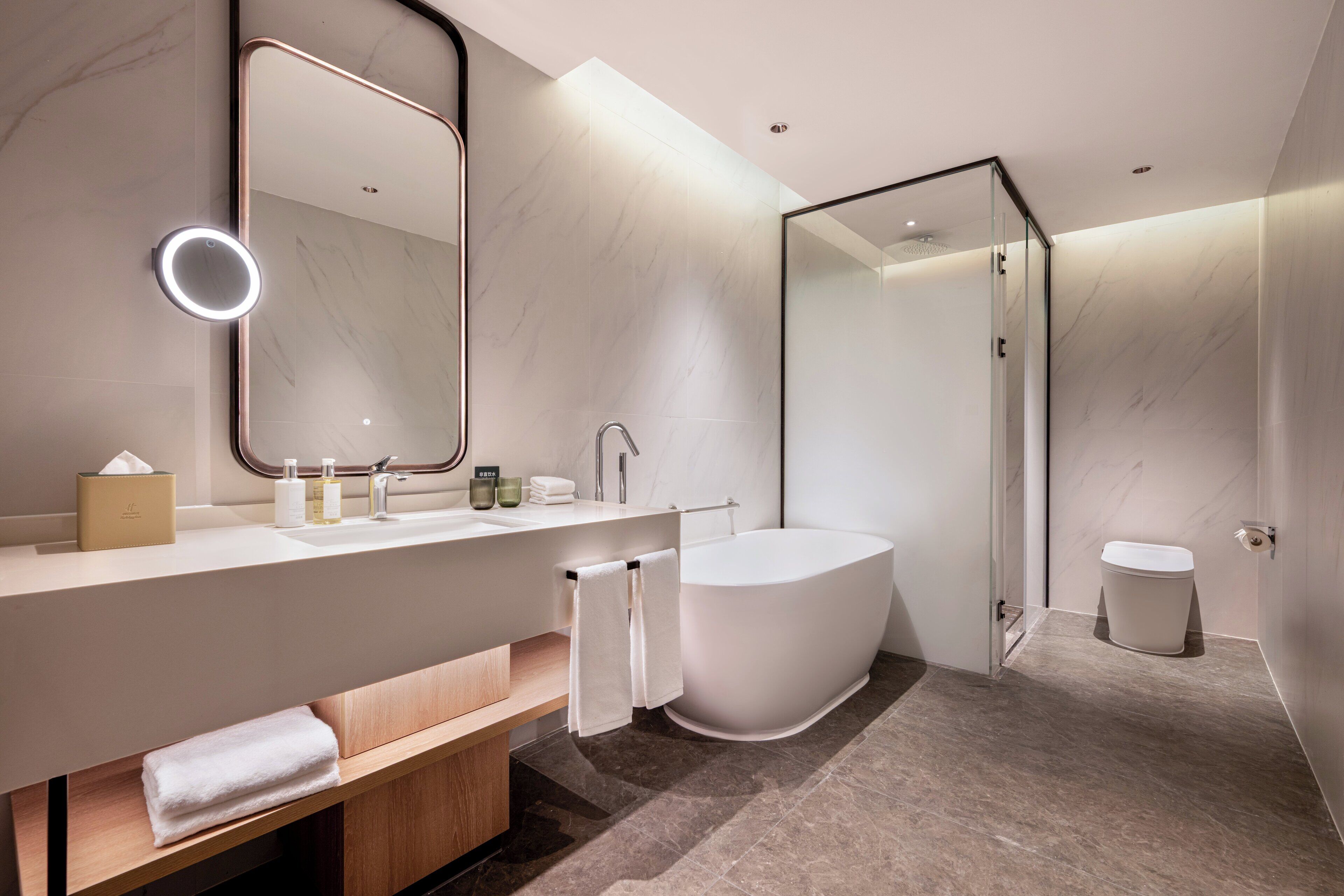 A modern bathroom with a large mirror, a bathtub, a toilet, and a vanity with a sink and towel rack.