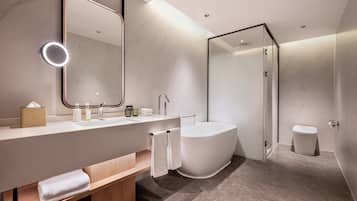 A modern bathroom with a large mirror, a bathtub, a toilet, and a vanity with a sink and towel rack.