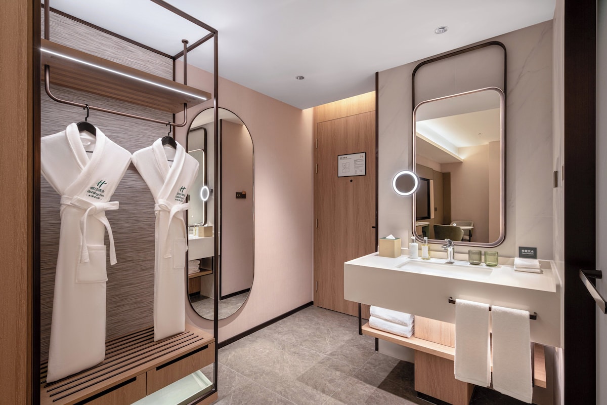 Un baño moderno con un tocador de madera, un espejo grande y dos batas blancas colgadas en un perchero.