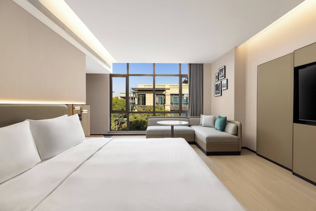 A modern hotel room with a large bed, a sofa, a small round table, and a TV.