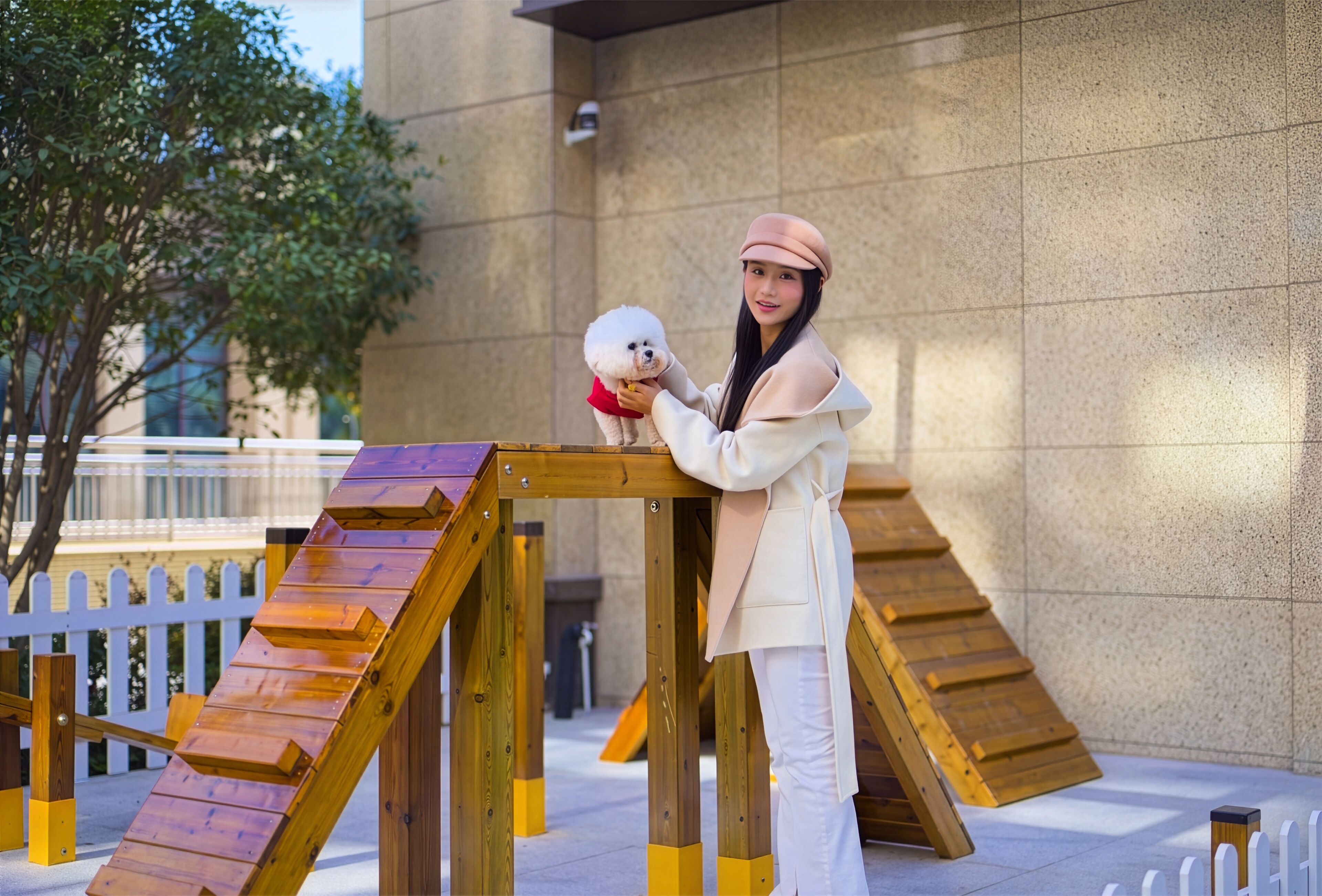 A person standing next to a wooden structure with a ramp, in front of a building with a stone facade.