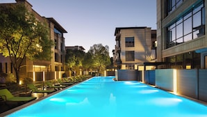 Una piscina con sillones de descanso y un edificio con ventanas amplias y balcones.