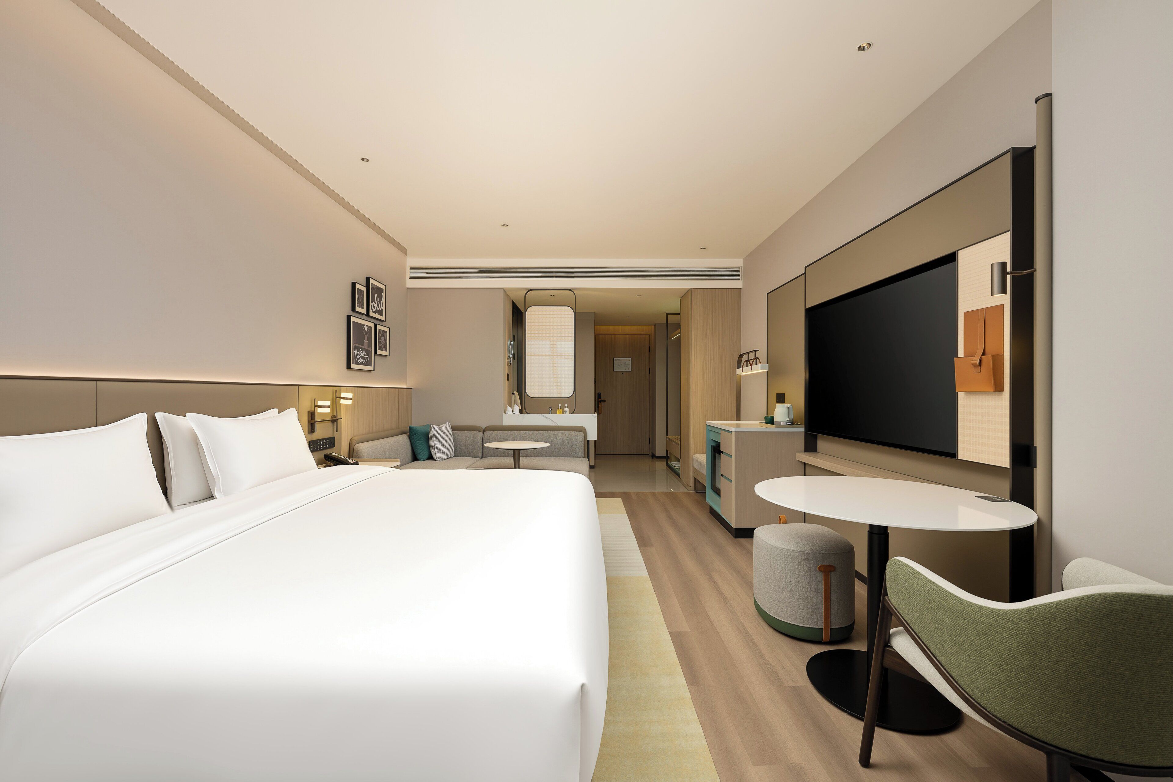A modern hotel room with a large bed, a small round table, a chair, a TV, and a mirror.