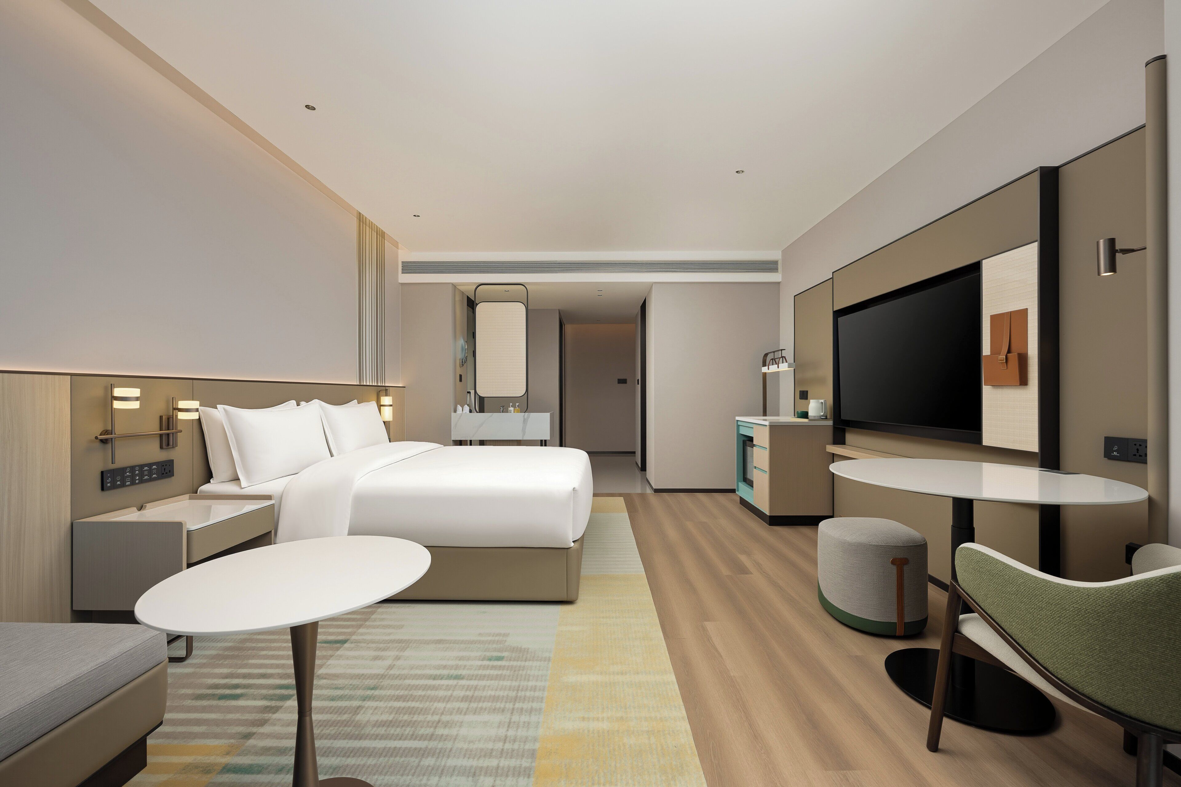 A modern hotel room with a bed, bedside tables, a TV, a small round table, and a green chair.