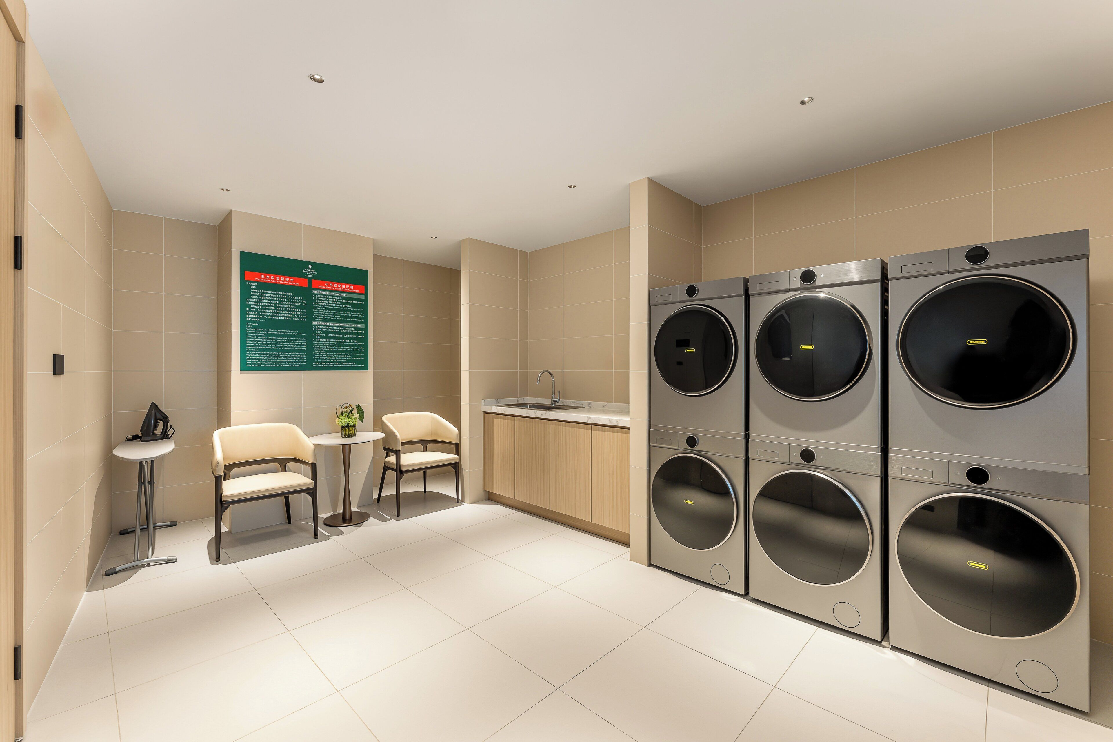 A modern laundry room with four stacked washing machines, a small table with a chair, and a bulletin board.