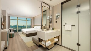Una habitación de hotel moderna con una cama grande, un espacio para sentarse, un baño con un espejo amplio y vistas a la ciudad.