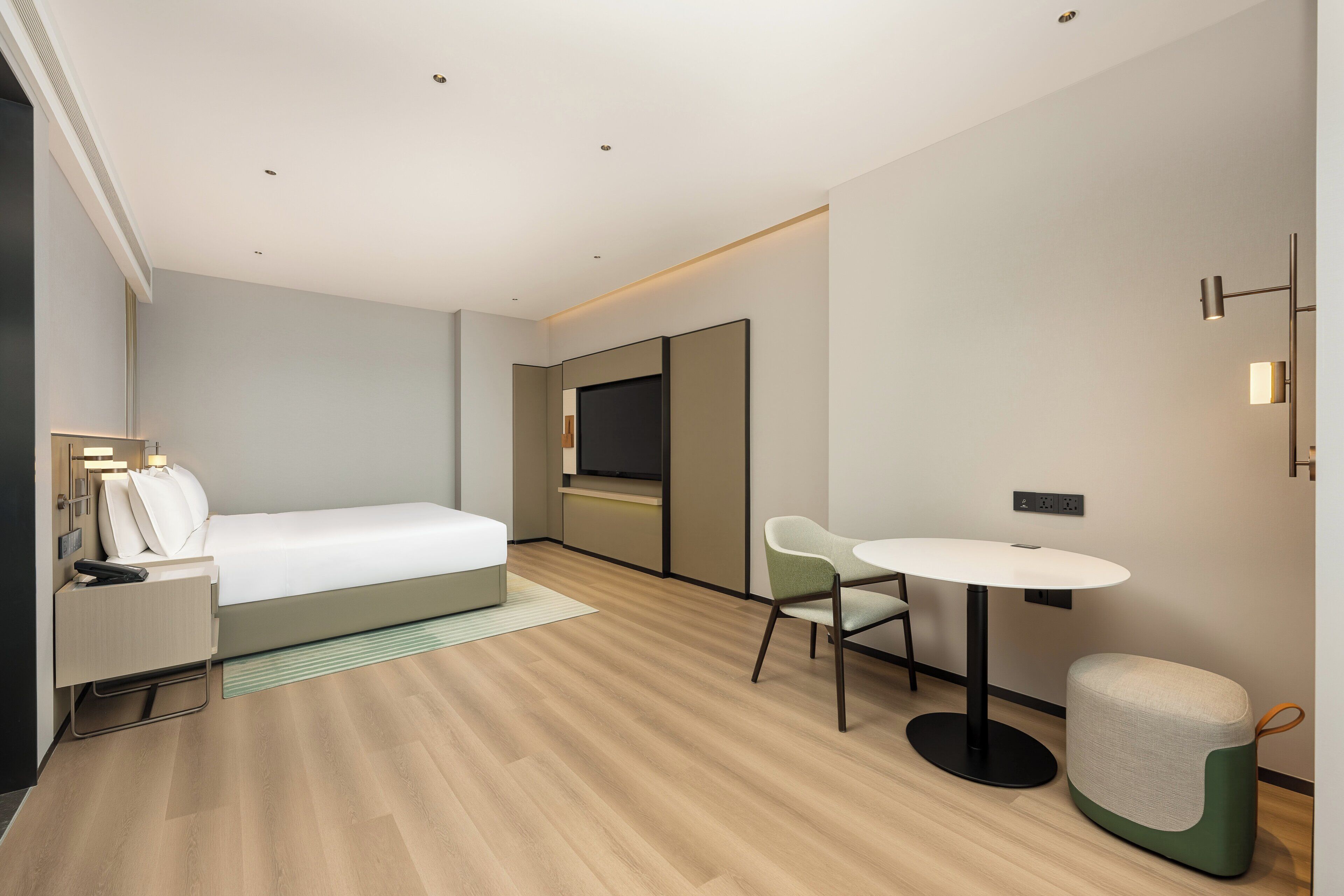 A modern hotel room with a bed, bedside table, chair, and a small round table.