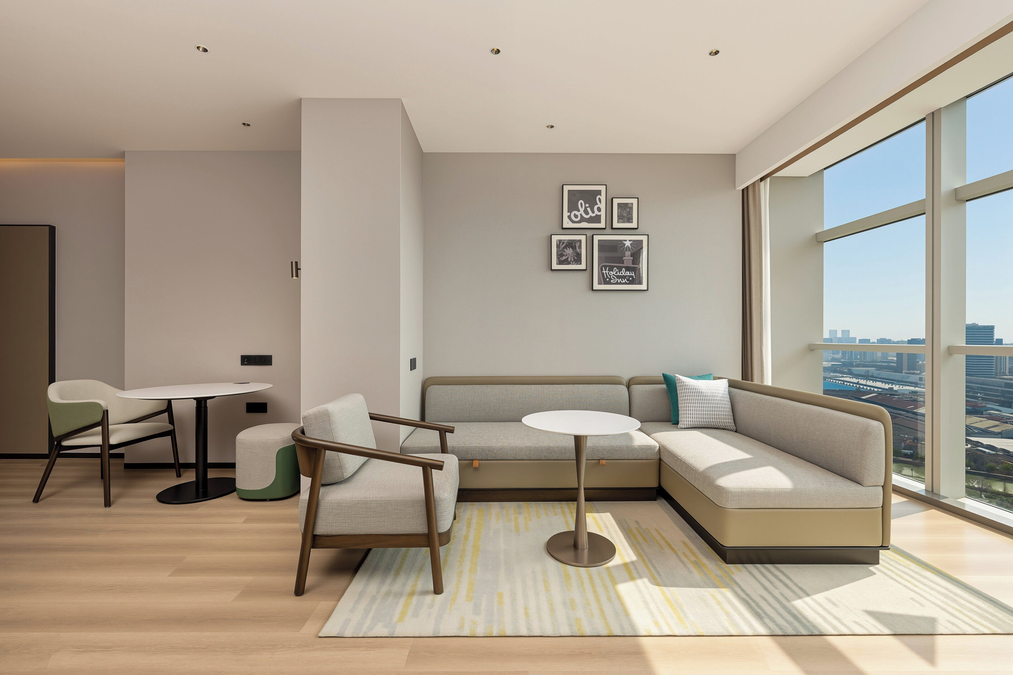 A modern living room with a sofa, chairs, a small table, and a large window offering a city view.
