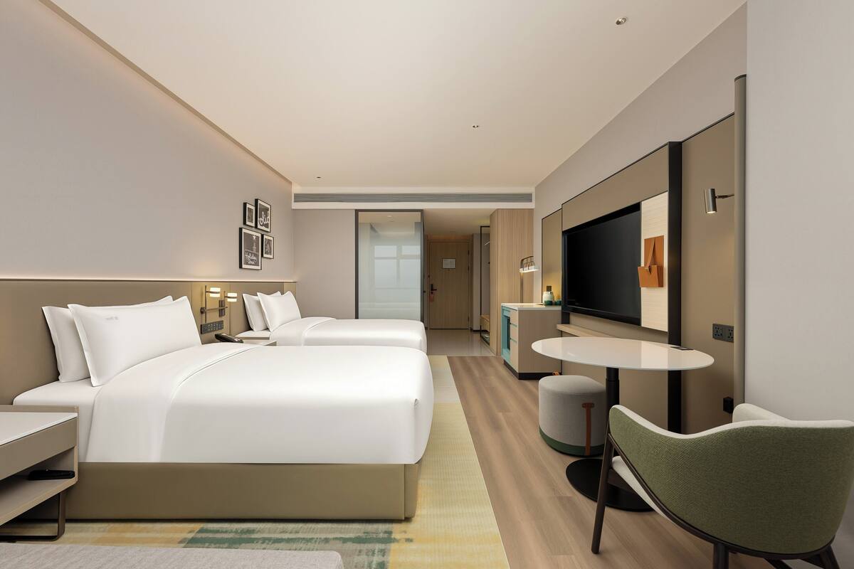 A modern hotel room with a large bed, a desk, a chair, a TV, and a small table.