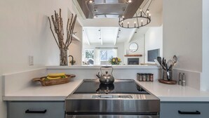 Una cocina moderna con estufa de acero inoxidable, un hervidor y un bol con fruta en la encimera.