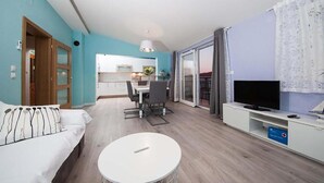 Ein modernes Wohnzimmer mit einer Couch, einem runden Couchtisch, einem Fernseher und einer Küche im Hintergrund.