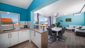 Eine moderne Küche mit Meerblick, ein Essbereich mit Tisch und Stühlen sowie ein Wohnbereich mit Sofa und Pflanze.
