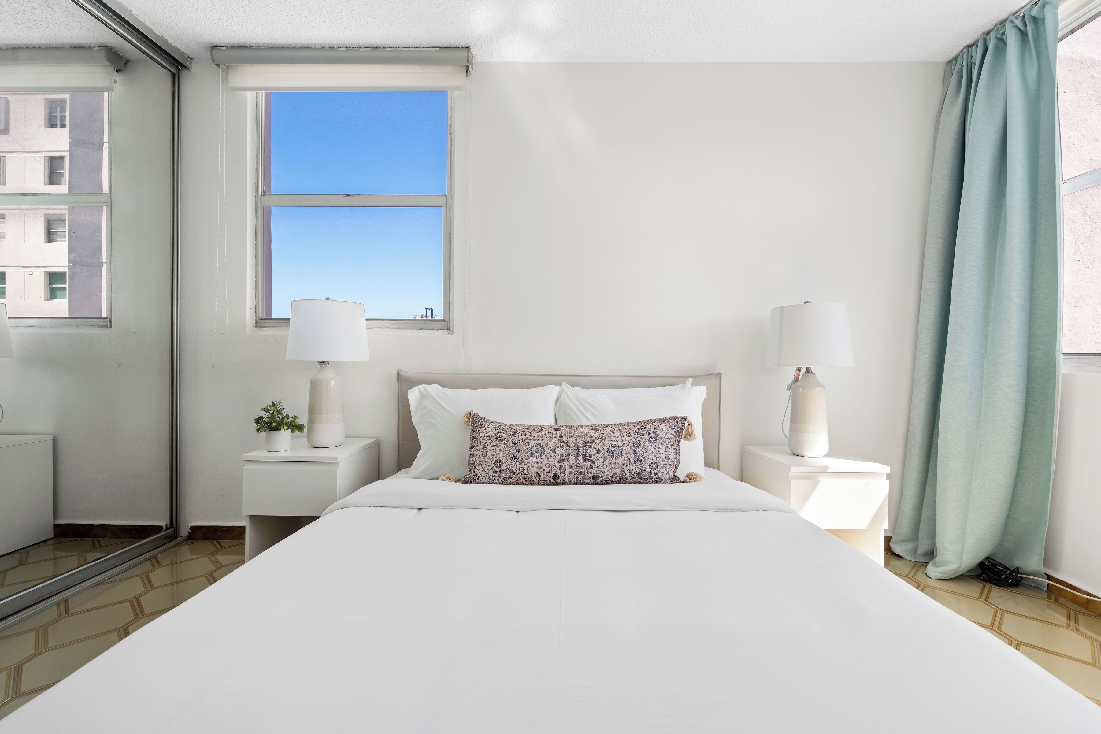 Een hotelkamer met een groot bed, twee nachtkastjes, een raam met uitzicht en een gordijn.