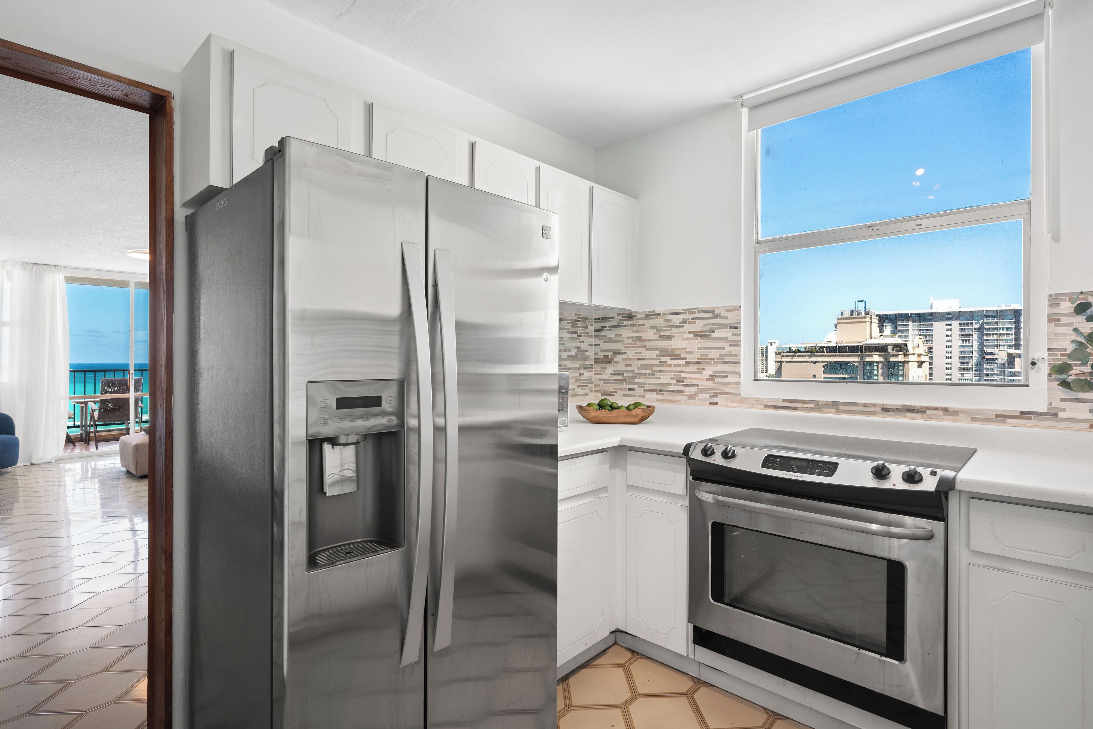 A modern kitchen with a stainless steel refrigerator, built-in oven, and a large window with a city view.