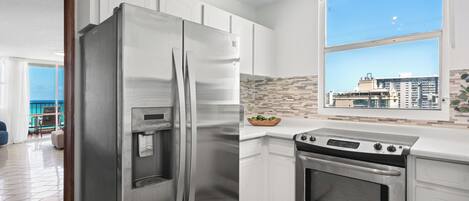 A modern kitchen with a stainless steel refrigerator, built-in oven, and a large window with a city view.