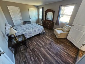 A bedroom with a bed, dresser, chair, and a large mirror. - Gran Lin - 5 bedroom - 8 beds (Saint Charles)