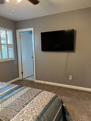Ein Schlafzimmer mit einem Bett, einem an der Wand montierten Fernseher und einer Tür zu einem anderen Raum.