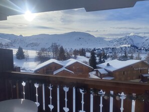Une cabane en bois, dont le toit est recouvert de neige, entourée de montagnes et sous un ciel dégagé.