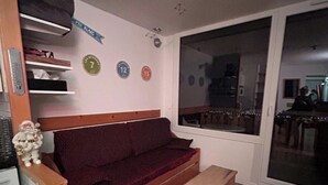 Ett vardagsrum med en soffa i trä, ett litet träbord och en skjutdörr i glas som leder till en matplats.