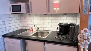 Ett kompakt kök med mikrovågsugn, diskho och kaffebryggare.