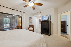 A bedroom with a large bed, a ceiling fan, a dresser, a television, and a sliding glass door leading to a balcony. - Desert Haven - Relax living, Pool, Tennis, Gated Community (Scottsdale)