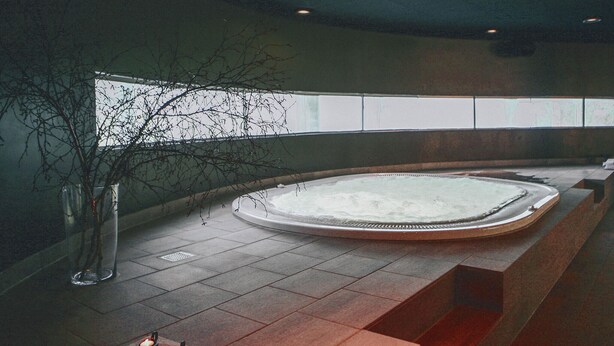 A spa area with a hot tub, a vase with branches, and candles on a wooden bench. - Lübker Golf og Spa Resort (Nimtofte)
