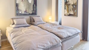 A double bed with a textured duvet and matching pillows, a bedside table with a lamp, and abstract art on the walls. - Lübker Golf og Spa Resort (Nimtofte)