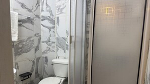 Et badeværelse med toilet, brusebad og vægge med marmorlook.