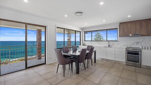 A modern kitchen with a view of the ocean, a dining area with a table and chairs, and a built-in oven. - Casa al mare - Ocean View Suite (Ulladulla)