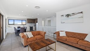 A spacious living area with two brown sofas, a wooden coffee table, and a dining area with a view. - Casa al mare - Ocean View Suite (Ulladulla)