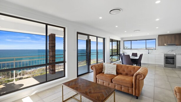 A spacious living area with a large window overlooking the ocean, a modern kitchen, and a comfortable seating area. - Casa al mare - Ocean View Suite (Ulladulla)